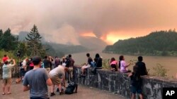 This photo, provided by Inciweb, shows people at a viewpoint overlooking the Columbia River watching the Eagle Creek wildfire burning in the Columbia River Gorge east of Portland, Ore., Sept. 4, 2017. A lengthy stretch of highway Interstate 84 remains closed as crews battle the growing Eagle Creek wildfire that has also caused evacuations and sparked blazes across the Columbia River in Washington state.