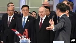 চীনের হারবিন শহরে এক বাণিজ্য প্রদর্শনীতে চীনের ভাইস প্রেসিডেন্ট হান জেং (মাঝে) এর সাথে রাশিয়ার প্রেসিডেন্ট প্রেসিডেন্ট পুতিন। ফাইল ফটোঃ ১৭ মে, ২০২৪। 