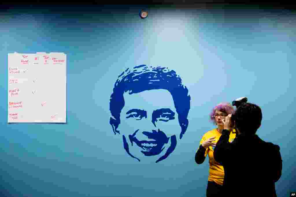 A supporter is interviewed next to a stencil of Democratic presidential candidate former South Bend, Ind., Mayor Pete Buttigieg at a campaign office on the day of the Iowa Caucus, Feb. 3, 2020.