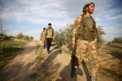 FILE - Turkey-backed Syrian fighters walk down a road in the town of Qirata, Syria, Dec. 24, 2018.