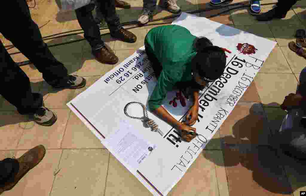 A woman writes on a poster demanding death by hanging for the four men convicted in the fatal gang rape of a young woman on a New Delhi bus last year, outside a court in New Delhi, Sept. 11, 2013. 