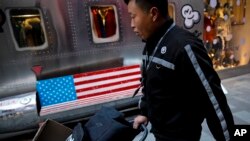 A delivery worker pushes a cart loaded with goods past by a bench with an American flag outside a fashion boutique selling U.S. brand clothing at the capital city's popular shopping mall in Beijing, Feb. 1, 2019. 
