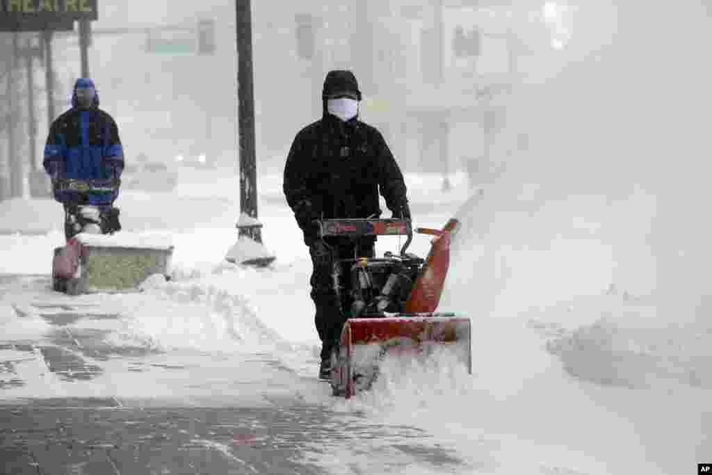 Para pekerja mencoba membersihkan salju dari trotoar dalam badai salju di Boston (27/1). ​(AP/Steven Senne)