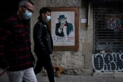 People walk past a poster that reads 'I want you to stay home', by artist TvBoy amid a lockdown in Barcelona, Spain, Tuesday, March 24, 2020. More than 1.5 billion around the world have been told to stay in their homes. (AP Photo/Felipe Dana)