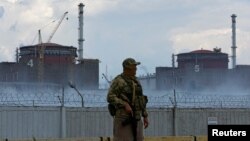 ទាហាន​ម្នាក់​ដែល​ស្លៀកពាក់​ឯកសណ្ឋាន​​ដោយ​មាន​ទង់ជាតិ​រុស្ស៊ី​ប៉ាក់ពី​លើ​​ឈរ​យាម​រោងចក្រ​នុយក្លេអ៊ែរ Zaporizhzhia នៅ​ខាង​ក្រៅ​ទីក្រុង Enerhodar ដែល​រុស្ស៊ី​កាន់កាប់​ក្នុង​តំបន់ Zaporizhzhia ប្រទេស​អ៊ុយក្រែន ថ្ងៃទី ៤ ខែសីហា ឆ្នាំ២០២២។ 