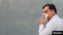 A man uses his handkerchief to cover his face as he walks on a road on a smoggy morning in New Delhi, Nov. 11, 2019.
