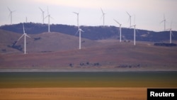 FILE - A fence is seen in front of wind turbines that are part of the Infigen Energy Capital Wind Farm located on the hills surrounding Lake George, near Canberra, Feb. 21, 2018.