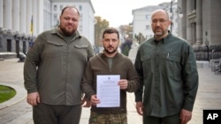 In a photo from Ukraine's Presidential Press Office, President Volodymyr Zelenskyy, center, with Prime Minister Denys Shmyhal, right, and head of the Supreme Council of Ukraine Ruslan Stefanchuk, holds an application for ''accelerated accession to NATO'' in Kyiv, Sept. 30, 2022. 