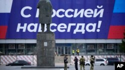 Russian servicemen patrol a street next to a statue of Soviet Union founder Vladimir Lenin, with a poster reading 'With Russia forever!' in the background, in Luhansk, Ukraine, Sept. 28, 2022.