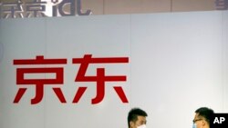 FILE - Visitors wearing face masks talk near a display for Chinese online retailer JD.com at the China International Fair for Trade in Services (CIFTIS) in Beijing, Sept. 2, 2022.