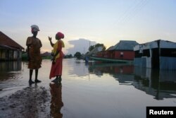 FILE - Two women wait for a canoe as floodwater overflows streets in Wadata in Makurdi, Nigeria, Oct. 1, 2022.