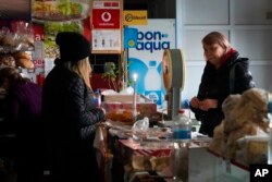 A local resident buys food products over a shop counter, lit by a candle, on the outskirts of Bakhmut, the site of the heaviest battle against the Russian troops in the Donetsk region, Ukraine, Friday, Oct. 28, 2022.