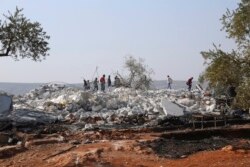 People look at a destroyed houses near the village of Barisha, in Idlib province, Syria, Oct. 27, 2019, after an operation by the U.S. military which targeted Abu Bakr al-Baghdadi, the shadowy leader of the Islamic State group.