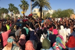 FILE - Sudanese demonstrators flash the victory sign as a military police vehicle drives past them during a protest demanding Sudanese President Omar Al-Bashir step down in Khartoum, Sudan, April 6, 2019.