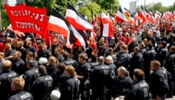 FILE - Riot police watch as far-right supporters take part in an anti-refugee rally in Dortmund, Germany, June 4, 2016. A placard in front reads, "Stop the flood of asylum seekers."