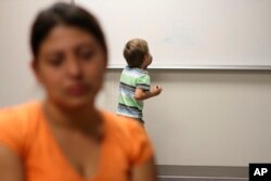 FILE - An unidentified immigrant from Guatemala is interviewed while her son paints on a whiteboard at the Artesia Family Residential Center, a federal detention facility, Sept. 10, 2014.