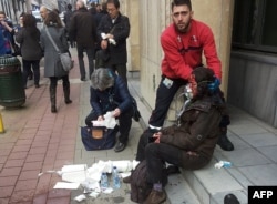 A private security guard helps a wounded women outside the Maalbeek metro station in Brussels on March 22, 2016 after a blast at this station located near the EU institutions.