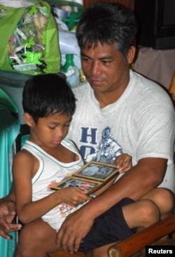 FILE - Cedric Caubalejo, 8, looks at a picture of his mother while sitting on his father's lap at their home in Manila, Oct. 19, 2006.