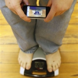 A man uses a smartphone to photograph and track his weight on a scale in his office in Pennsylvania