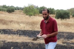 Ossama, a father of four, picks up bits of a rocket that hit farmland the night after Tripoli forces re-took the town from Khalifa Haftar's Libyan National Army, in Gharyan, Libya, June 28, 2019. (H.Murdock/VOA)