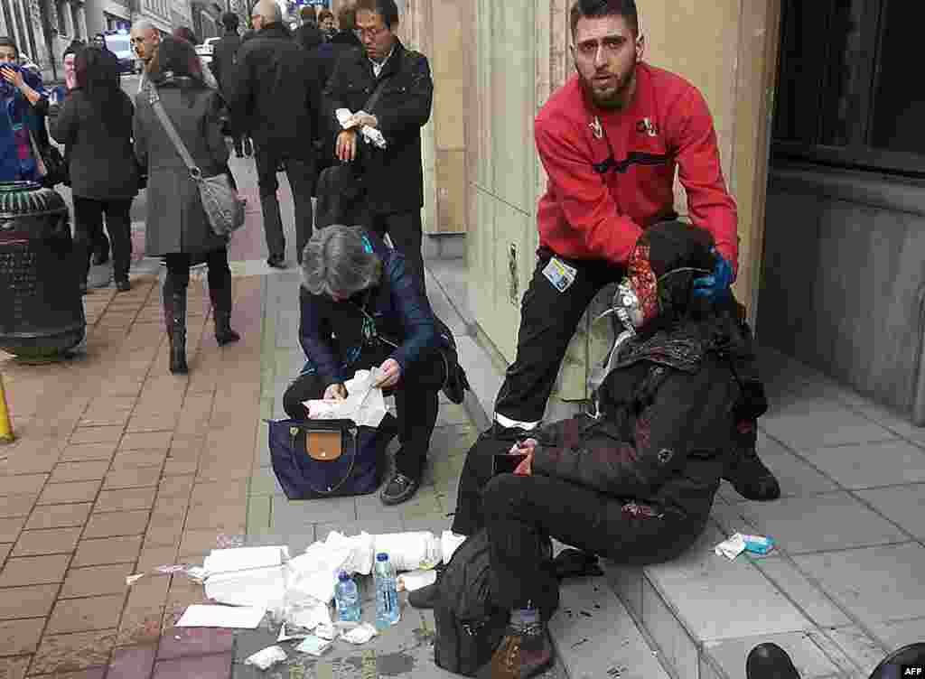 Seorang satpam menolong seorang perempuan yang terluka akibat ledakan di stasiun metro Maalbeek di Brussels (22/3). (AFP/Michael Villa)