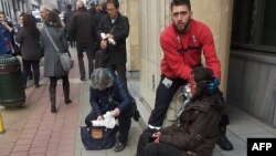 FILE - A private security guard helps a wounded woman outside the Maalbeek metro station in Brussels after a blast there March 22, 2016. The prime minister acknowledged security lapses but defended anti-terror efforts. 