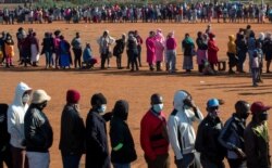 FILE - People affected by the coronavirus economic downturn line up to receive food aid in Pretoria, South Africa, May 20, 2020.
