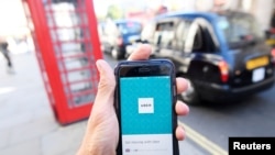 FILE - A photo illustration shows a London taxi passing as the Uber app logo is displayed on a mobile phone, as it is held up for a posed photograph in central London, Britain, Sept. 22, 2017.