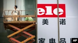 Para kerja memasang spanduk untuk pembukaan sebuah toko elektronik di Beijing (15/7). (AP/Mark Schiefelbein)