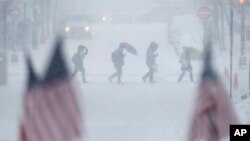 People walk across a snow-covered intersection behind American flags in Hoboken, New Jersey, Feb. 9, 2017.