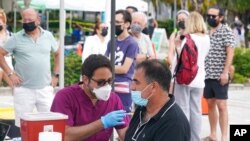 FILE - Carlos Anacleto, right, closes his eyes as he receives a shot of the Pfizer COVID-19 vaccine from nurse Jorge Tase, as others wait their turn, Aug. 4, 2021, in Miami Beach, Florida. 