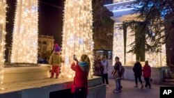People take pictures at Nakhimov's Square in Sevastopol, Crimea. As New Year’s Eve approaches, the central square of Crimea’s largest city is festooned with lighted holiday decorations, including a soaring artificial tree that flashes and winks. But areas a few steps away are sunk in darkness, the streetlamps turned off because of an electricity shortage, Dec. 27, 2015.