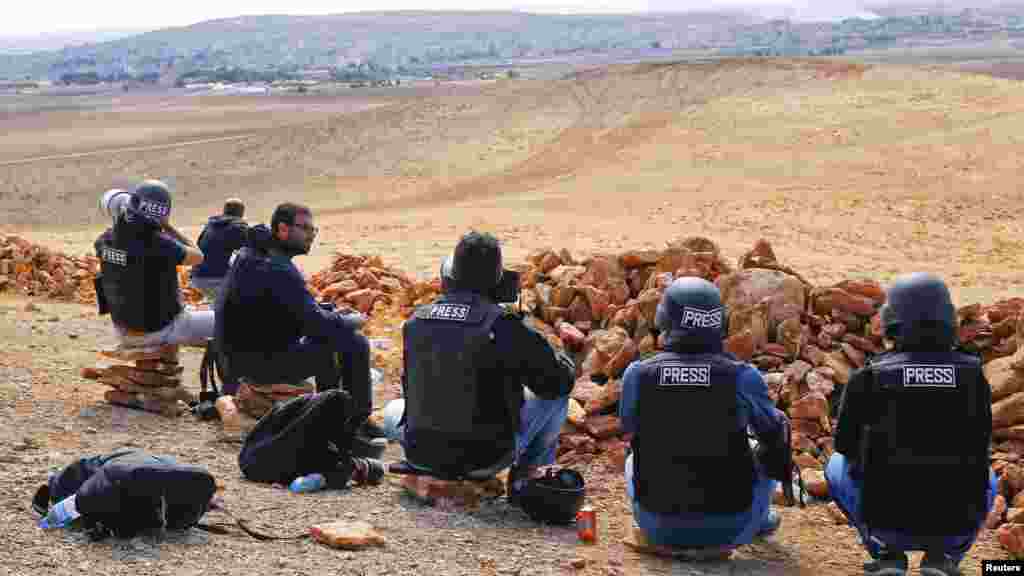 Photographers and members of the media watch the Syrian town of Kobani from atop a hill on the Turkish-Syrian border, Oct. 15, 2014. 