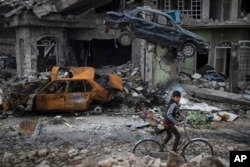 A boy rides his bike past destroyed cars and houses in a neighborhood recently liberated by Iraqi security forces, on the western side of Mosul, Iraq, Sunday, March 19, 2017.