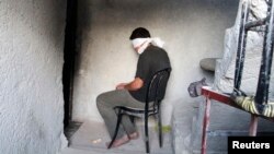 FILE - A blindfolded man suspected of passing on military information to the Syrian government waits to be interrogated after being arrested by Free Syrian Army (FSA) fighters, inside an FSA-run prison in Aleppo.