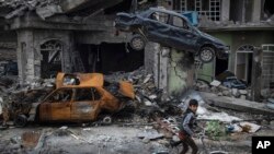 A boy rides his bike past destroyed cars and houses in a neighborhood recently liberated by Iraqi security forces, on the western side of Mosul, Iraq, Sunday, March 19, 2017.