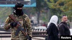 Луѓе поминуваат покрај бунтовнички борец кој чува стража на плоштад, откако бунтовниците го зазедоа главниот град и го соборија претседателот Башар ал-Асад, во Дамаск, Сирија, 11 декември 2024 година