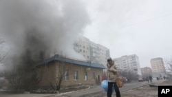 ស្រ្តី​ម្នាក់​ដើរ​កាត់​ផ្ទះ​ឆេះ​មួយ​ក្នុង​តំបន់​ Mariupol ក្នុង​ប្រទេស​អ៊ុយក្រែន កាល​ពី​ថ្ងៃ​សៅរ៍ ទី​២៤ ខែ​មករា ឆ្នាំ​២០១៥។