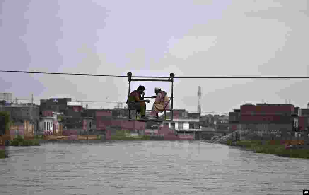 Dua orang Pakistan ngobrol sambil menyeberangi sungai, menggunakan &#39;jembatan&#39; yang dioperasikan dengan tali di pinggiran Islamabad.