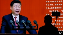 FILE - A man takes a selfie near a picture of Chinese President Xi Jinping at an exhibition on the Long March at the military museum in Beijing, Oct. 24, 2016.