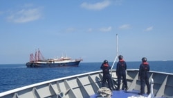 FILE PHOTO: Philippine Coast Guard personnel survey several ships believed to be Chinese militia vessels in Sabina Shoal in the South China Sea, in a handout photo distributed by the Philippine Coast Guard on May 5 and taken according to source on April 2