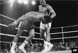 In this Oct. 30, 1974, file photo, challenger Muhammad Ali watches as defending world champion George Foreman goes down to the canvas in the eighth round of their WBA/WBC championship match in Kinshasa, Zaire.