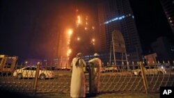 Two Emirati officials watch a high-rise building as a fire spreads up the side of the building in Ajman, United Arab Emirates, March 29, 2016. 