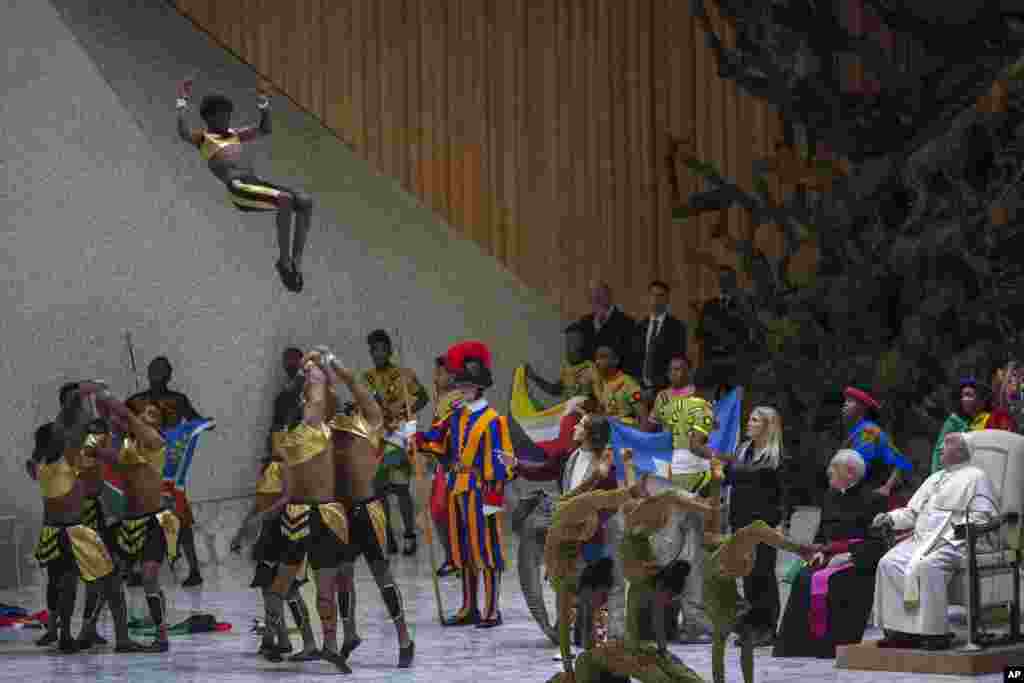 Pope Francis, right, looks at a performance by CircAfrica circus troupe during the weekly general audience in the Paul VI Hall, at the Vatican.
