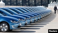 FILE - People walk past row of Volkswagen e-Golf cars during the company's annual news conference in Berlin, March 13, 2014.
