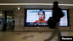 Seseorang di Tokyo berjalan melewati layar televisi yang menayangkan wajah sandera ISIS dari Jepang, Kenji Goto.