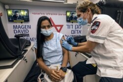 FILE - A medic with Israel's Magen David Adom emergency service administers a booster shot of a COVID-19 vaccine to a woman in Tel Aviv, Aug. 14, 2021.