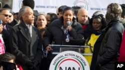Pendeta Al Sharpton (kiri) mendengarkan janda Eric Garner, Esaw, berbicara dalam demonstrasi di Freedom Plaza, Washington, DC (13/12). (AP/Jose Luis Magana)