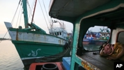 A fisherman sleeps on his boat as the vessel, left, used to carry Rohingya Muslims from Myanmar and migrants from Bangladesh is docked at a port in Lhokseumawe, Aceh province, Indonesia, Thursday, May 14, 2015.