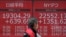 A man walks past an electronic stock board showing Japan's Nikkei 225 and New York Dow index at a securities firm in Tokyo Friday, March 27, 2020. Shares are mostly higher in Asia after stocks surged again on Wall Street with the approaching…